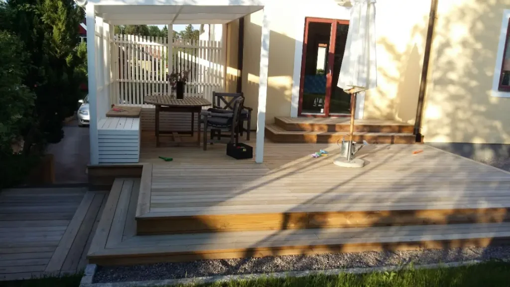 alt="Drewniany taras z zadaszeniem i stylowym oświetleniem przy domu jednorodzinnym"